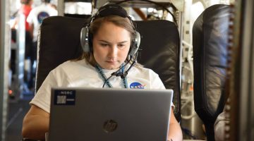 Honors student Laura Paye is shown wearing a headset, using a laptop, wearing a NASA tshirt