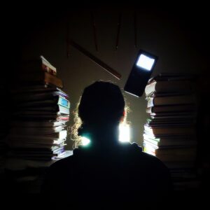 A photo of Zachary Scott surrounded by books, pencils, and a calculator, illuminated by the light of his computer screen.