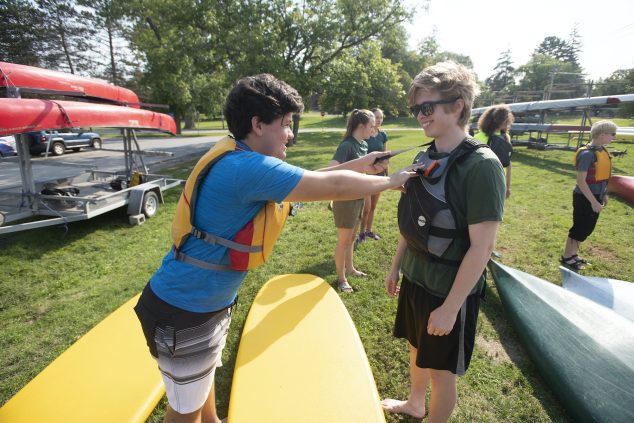 student helping other student put on life jacket