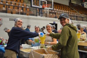 students wearing headnets pouring ingredients into a funnel at the Maine Day Meal Packout