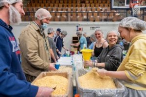 A group of students gathered around a table packing food for the Maine Day Meal Packout 